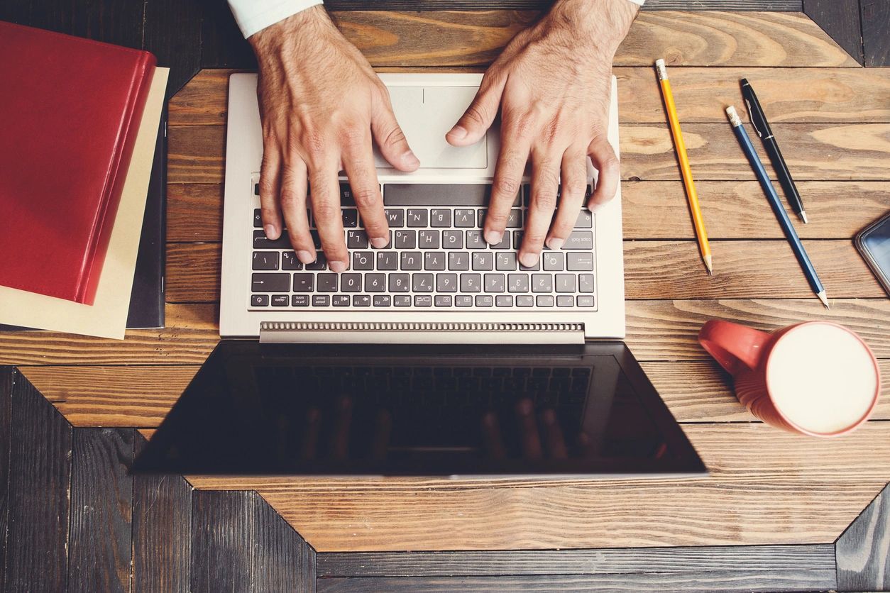 A person typing on a laptop with a pencil and ruler in the background.