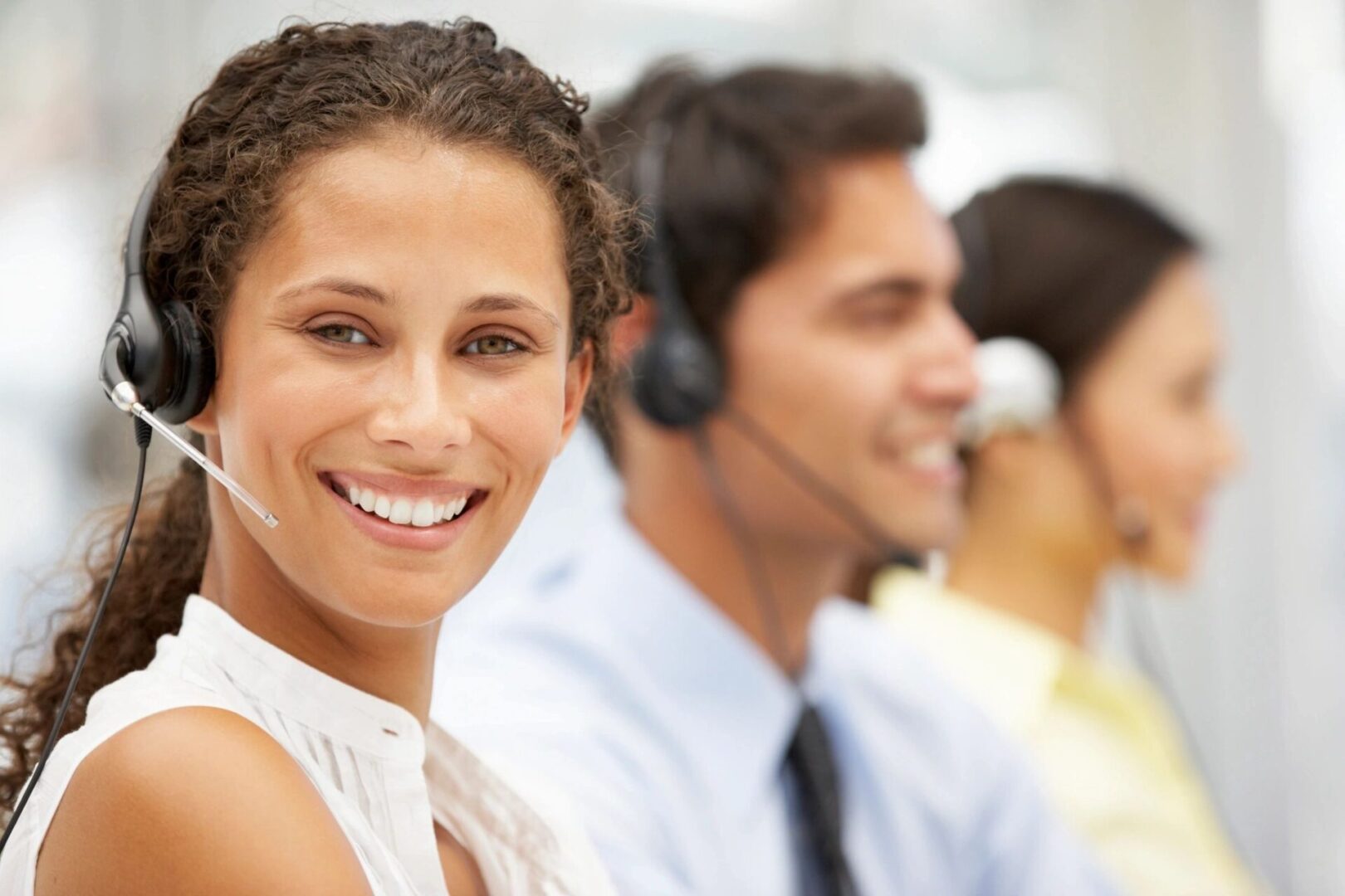 A woman smiles while wearing headphones and sitting in front of other people.